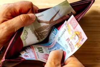 Person holding a red wallet open, exposing several colorful Mexican peso banknotes inside. Clarifies currency and wallet use.