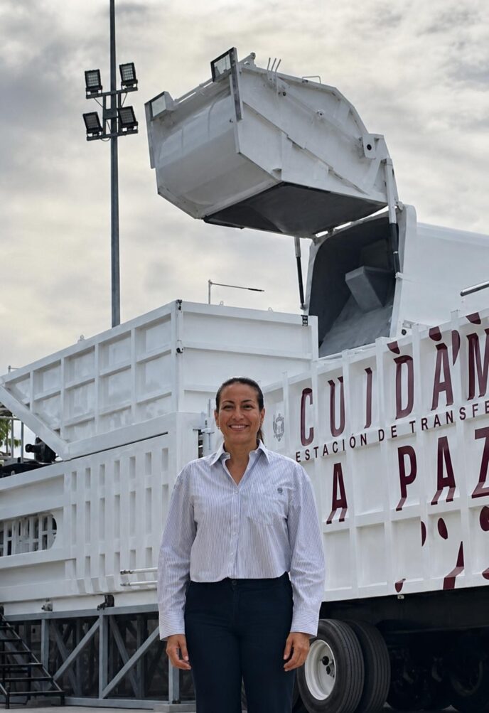 Smiling woman standing in front of a large white industrial truck with a raised hopper at a transfer station