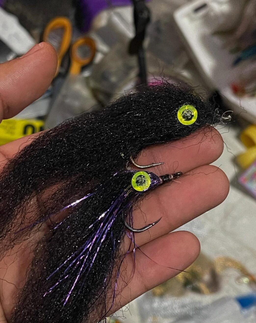 Close-up of a black hair-style fishing lure with yellow neon beads and sharp hooks held in a hand.