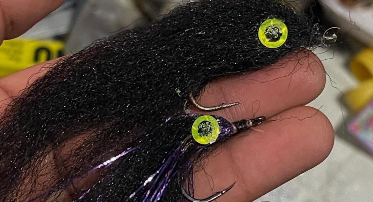 Close-up of a black hair-style fishing lure with yellow neon beads and sharp hooks held in a hand.
