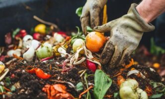 Gloved hands digging through a pile of colorful fruit and vegetable scraps for composting.