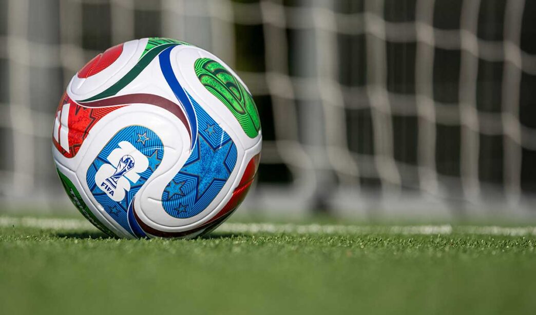 Colorful soccer ball on a green field with a blurred goal net in the background, marked with FIFA branding.