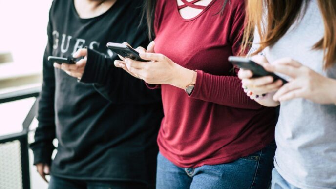 Three people standing together, each looking at a mobile phone