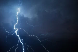 Bright lightning bolt forks through a dark stormy sky with blue tones.