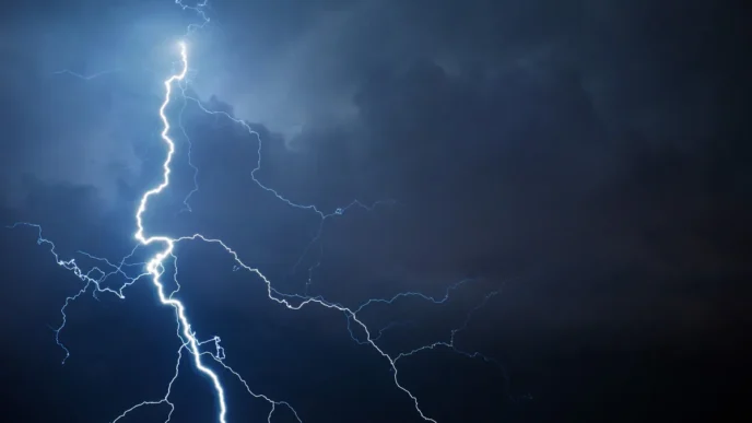 Bright lightning bolt forks through a dark stormy sky with blue tones.