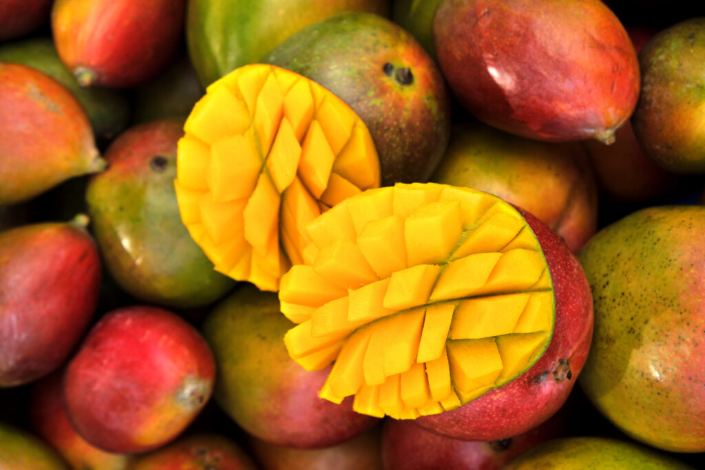 Close up fresh mango fruit on market stall - Gringo Gazette Ripe mangoes piled together, with one yellow mango cut into cubes in the foreground48?