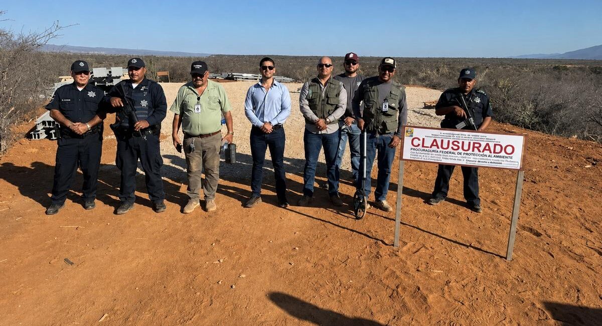 Group of uniformed officers posing in a dry desert landscape beside a 'CLAUSURADO' sign indicating area closure