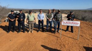 Group of uniformed officers posing in a dry desert landscape beside a 'CLAUSURADO' sign indicating area closure