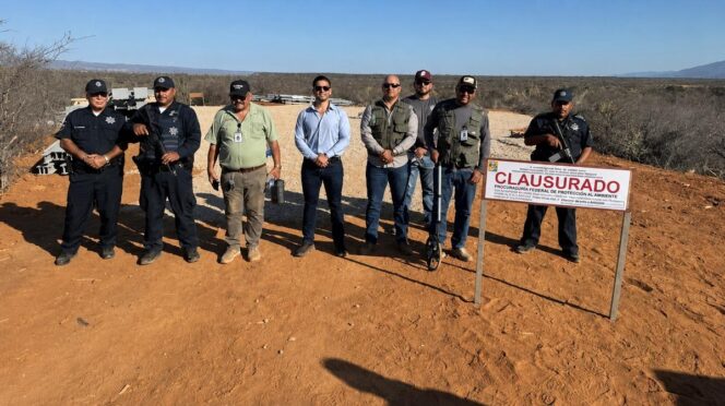 Group of uniformed officers posing in a dry desert landscape beside a 'CLAUSURADO' sign indicating area closure