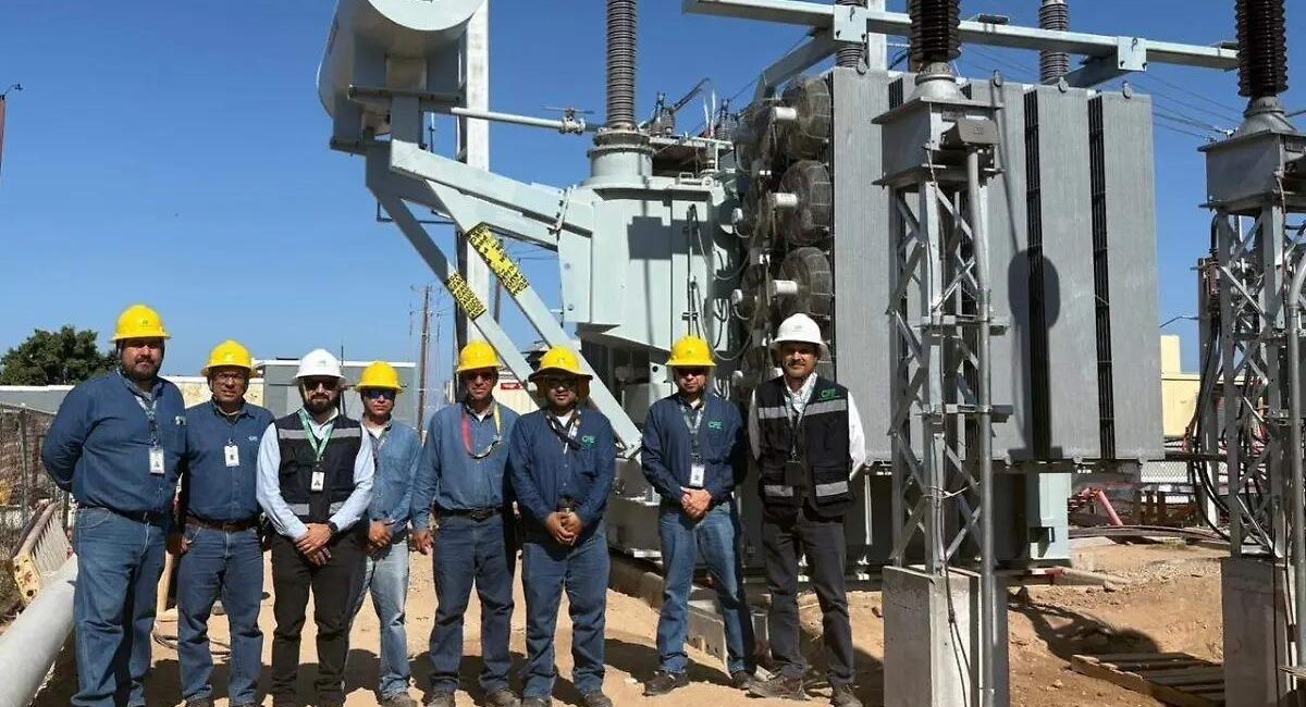 Group of utility workers in hard hats standing in front of large electrical transformers at a substation construction site
