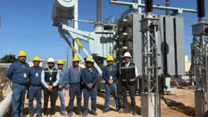 Group of utility workers in hard hats standing in front of large electrical transformers at a substation construction site