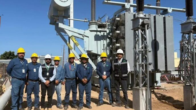 Group of utility workers in hard hats standing in front of large electrical transformers at a substation construction site