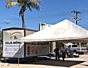 Mobile bank truck labeled Caja Móvil under a white canopy, with a palm tree and people nearby.