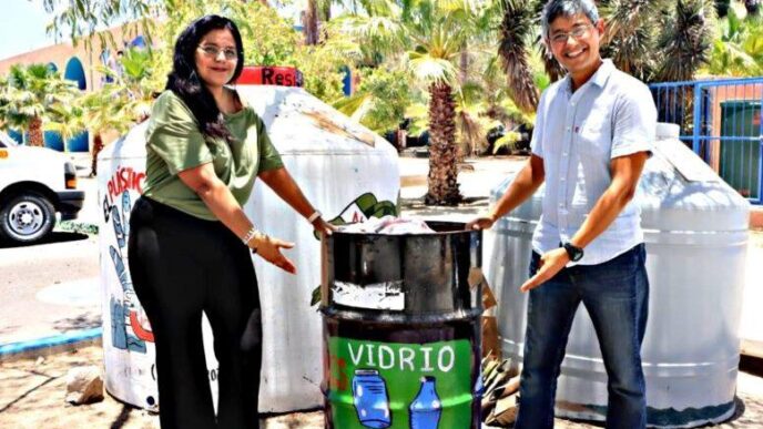 Two people stand beside a glass recycling bin labeled 'VIDRIO' showing bottles, outdoors with palm trees in the background.