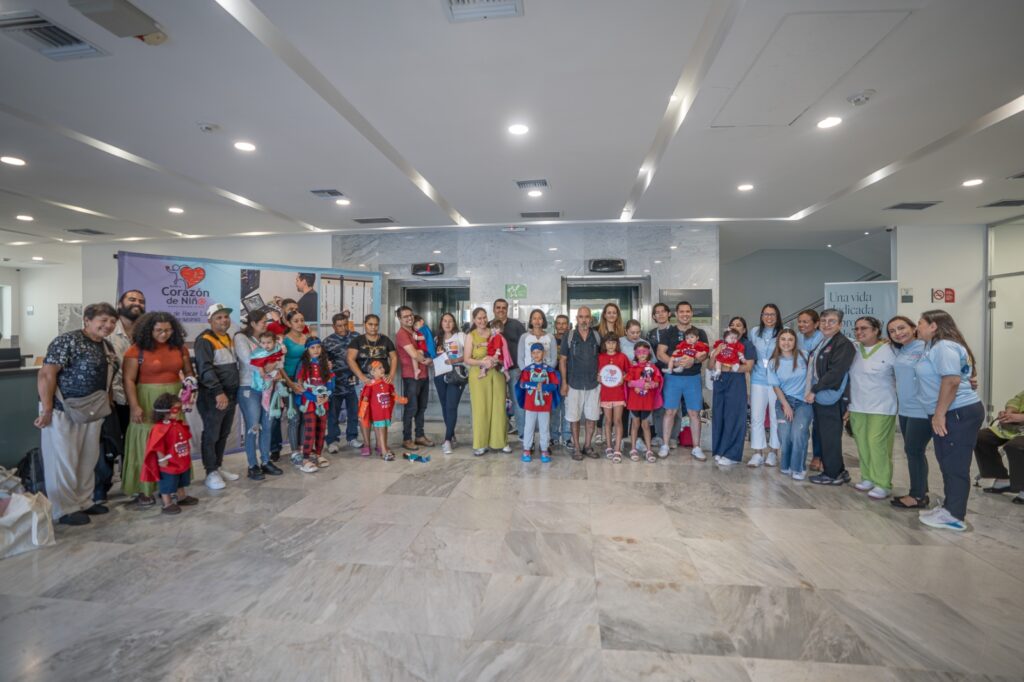 Large group of adults and children posing for a group photo in a bright, marble-floored lobby; a banner on the left reads 'Corazón de Niño'.