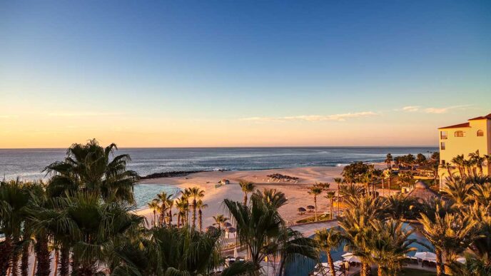 Sunset over a tropical beach with palm trees, a pool area in the foreground, and a calm sea beyond.