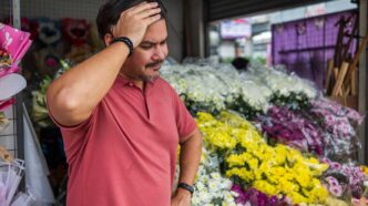 decliningSales - Gringo Gazette Man in a red polo shirt stands in a flower shop, hand on his forehead, looking pensive among colorful bouquets.