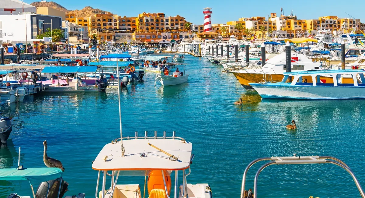 Busy marina with colorful boats docked along piers, turquoise water, and yellow buildings in the background.