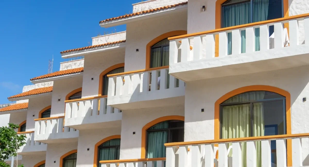 White Mediterranean-style apartment building with orange arches and balconies under a blue sky