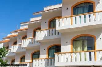 White Mediterranean-style apartment building with orange arches and balconies under a blue sky