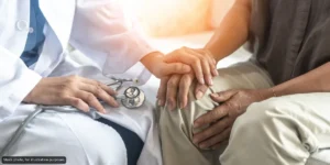 Doctor in a white coat holds a patient's hand, offering comfort and support during a check-up.