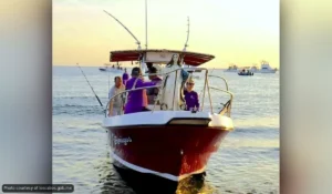 Group of people on a red boat fishing at sunset on calm water.