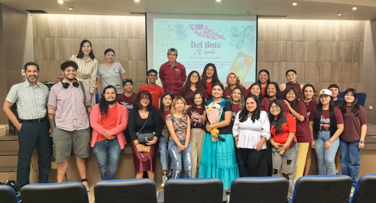 Group of about 25–30 people posing on a stage in a lecture hall, in front of a projected slide that says 'Del tinta'.