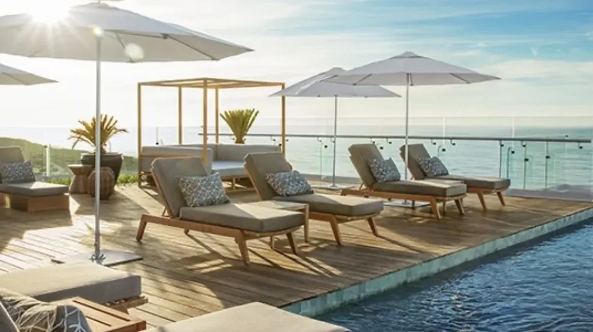 Poolside deck with cushioned lounge chairs under white umbrellas overlooking the ocean at sunset/early morning light? (informative: pool area with sea view)