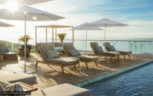 Poolside deck with cushioned lounge chairs under white umbrellas overlooking the ocean at sunset/early morning light? (informative: pool area with sea view)