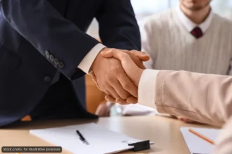Two professionals shake hands over a desk after signing, with papers and a pen visible on the table.
