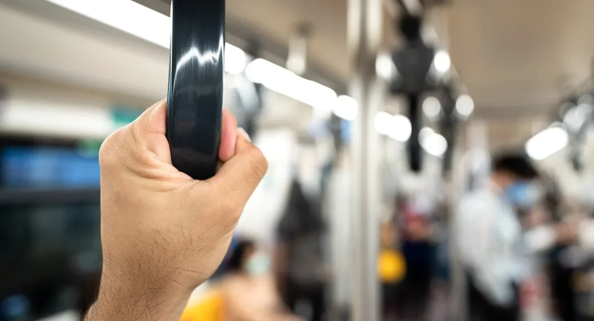 Person gripping a vertical handrail on a crowded subway car, blurred passengers in the background.