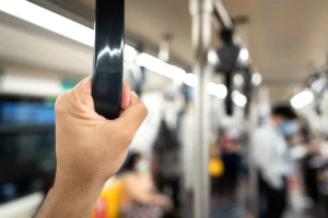 Person gripping a vertical handrail on a crowded subway car, blurred passengers in the background.