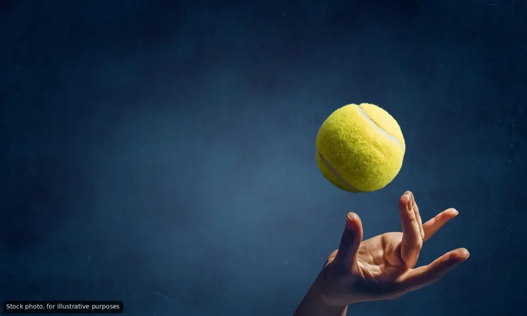 Tennis ball suspended midair above an open hand against a dark blue background