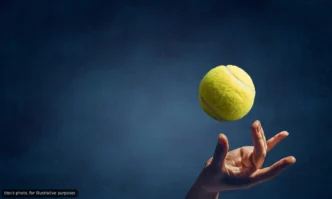 Tennis ball suspended midair above an open hand against a dark blue background