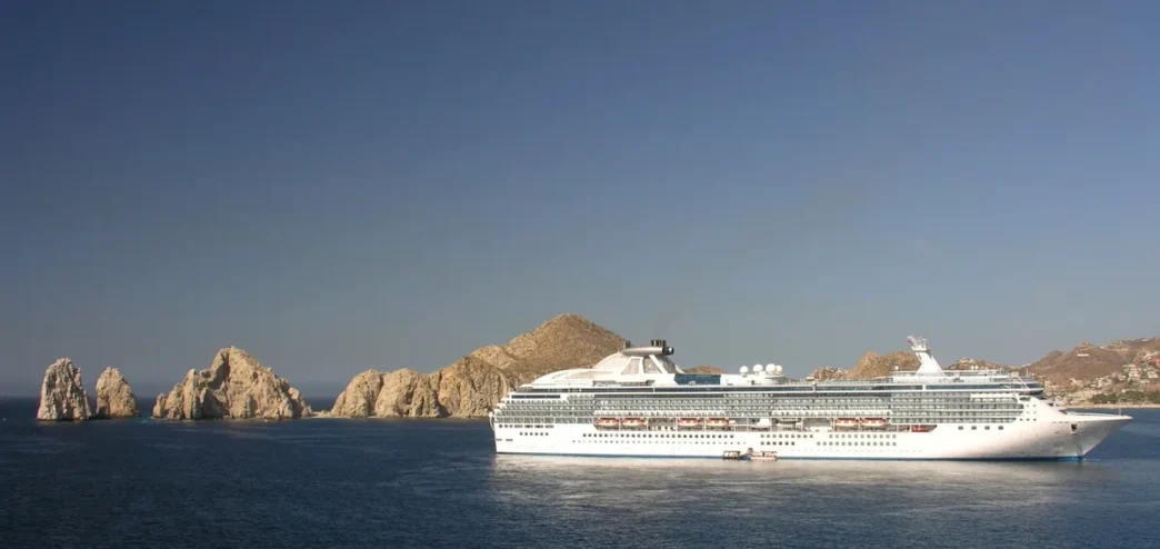Mexico Cruise Tourism Jumps 17% in First Half of 2026 - Gringo Gazette Large white cruise ship sailing near jagged rocky islets off a calm blue sea under a clear sky.