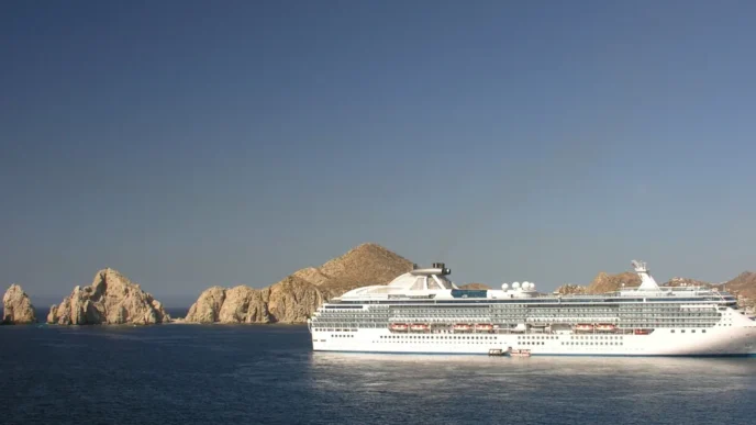 Large white cruise ship sailing near jagged rocky islets off a calm blue sea under a clear sky.