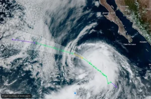 Satellite image of a hurricane off the western Mexican coast near Baja California, with the storm’s eye and spiral clouds visible and a colored forecast track overlay in purple, yellow, and green lines. Alternate: Storm with clear eye approaching Mexico’s Pacific coast; forecast path shown by multi-color lines.