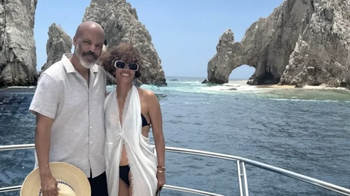 Halle Berry Celebrates 60th Birthday at Zadún in Los Cabos - Gringo Gazette Couple posing on a boat with a rocky sea arch and blue ocean behind them under a clear sky.