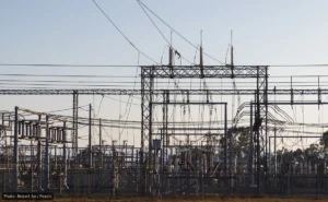 High-voltage electrical substation with metal lattice structures and a tangle of overhead power lines and insulators.