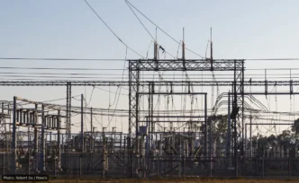 High-voltage electrical substation with metal lattice structures and a tangle of overhead power lines and insulators.