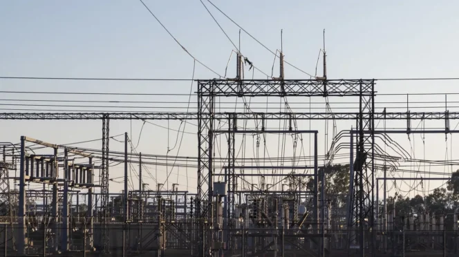 High-voltage electrical substation with metal lattice structures and a tangle of overhead power lines and insulators.