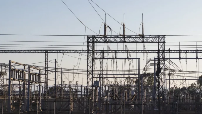 High-voltage electrical substation with metal lattice structures and a tangle of overhead power lines and insulators.