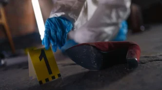 Forensic investigator in blue gloves places a yellow evidence marker labeled 1 beside a red high-heeled shoe on a dusty floor.