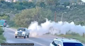 White smoke billowing from a roadside area as cars pass on a two-lane road used in a traffic scene.