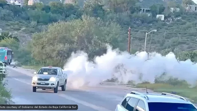 White smoke billowing from a roadside area as cars pass on a two-lane road used in a traffic scene.