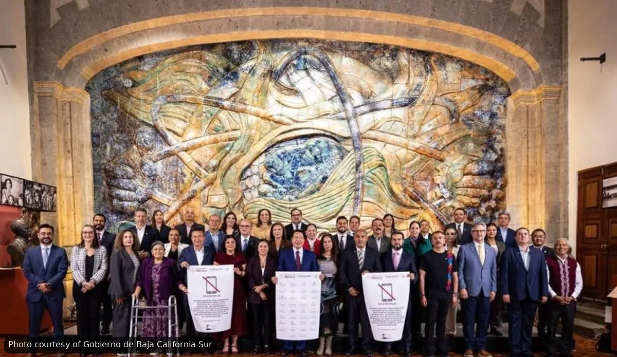 Group of officials in suits posing for a formal photo in a room with a large abstract mural behind them in warm tones.