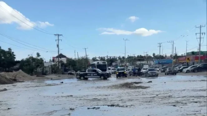 Urban street heavily flooded with muddy water; vehicles navigate through the water and a police pickup is in the foreground.