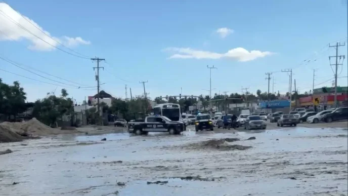 Urban street heavily flooded with muddy water; vehicles navigate through the water and a police pickup is in the foreground.