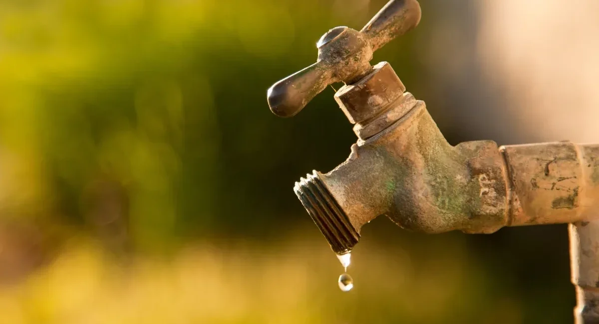 Rusty outdoor faucet dripping water drops, warm sunset background
