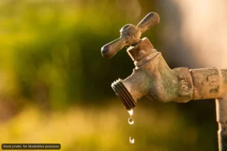 Rusty outdoor faucet dripping water drops, warm sunset background